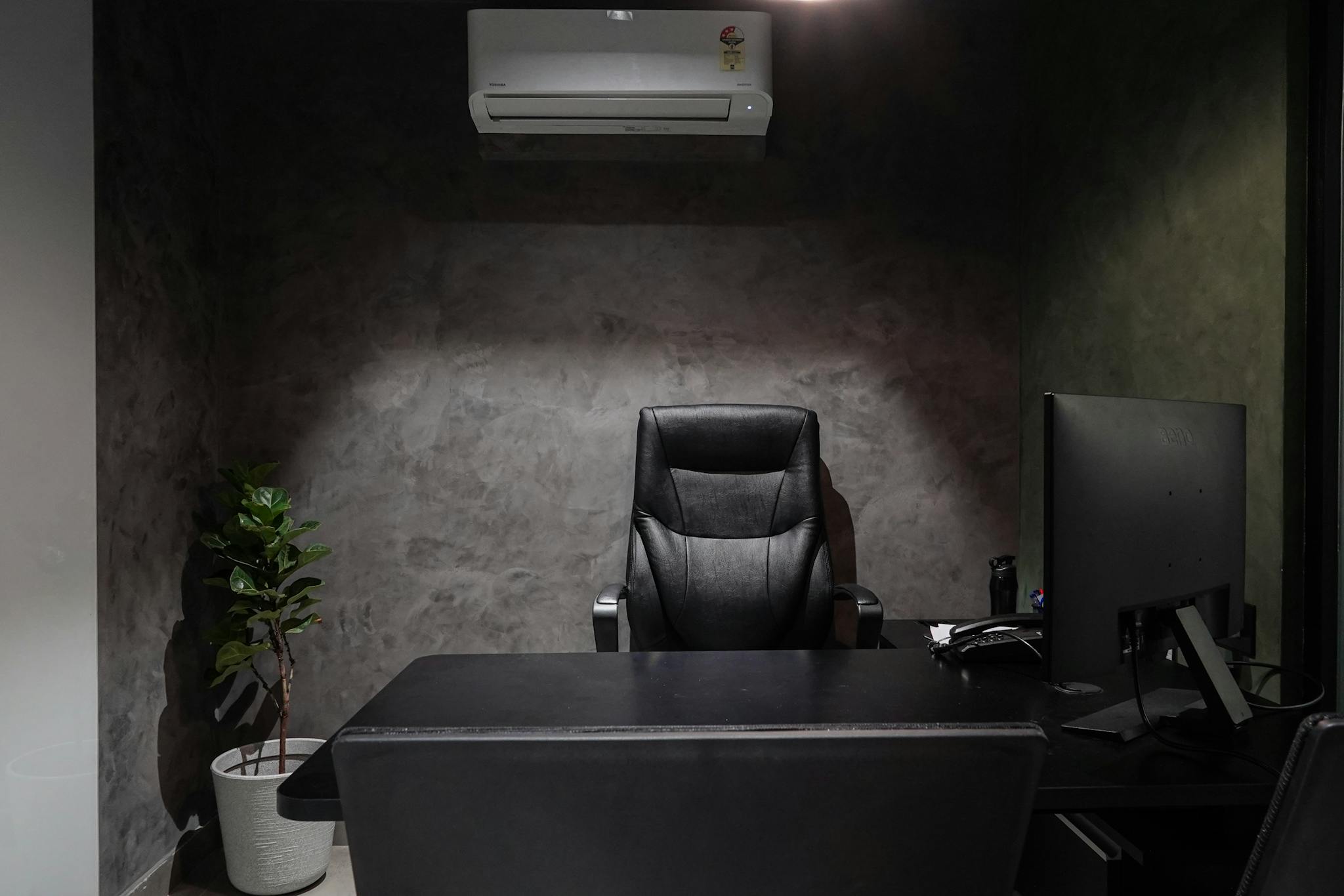 Minimalist office interior featuring leather chair, desk, monitor, plant, and air conditioner.